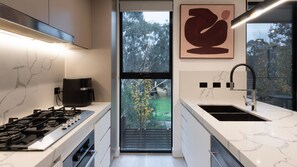 A modern kitchen with a gas stove, coffee maker, and a large window with a view of trees. - The Treetop Townhouse in Templestowe (Templestowe Lower)
