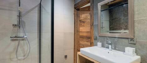 Ein modernes Badezimmer mit einer gläsernen Dusche, einem Holzkosmetikschrank und einem großen Spiegel.