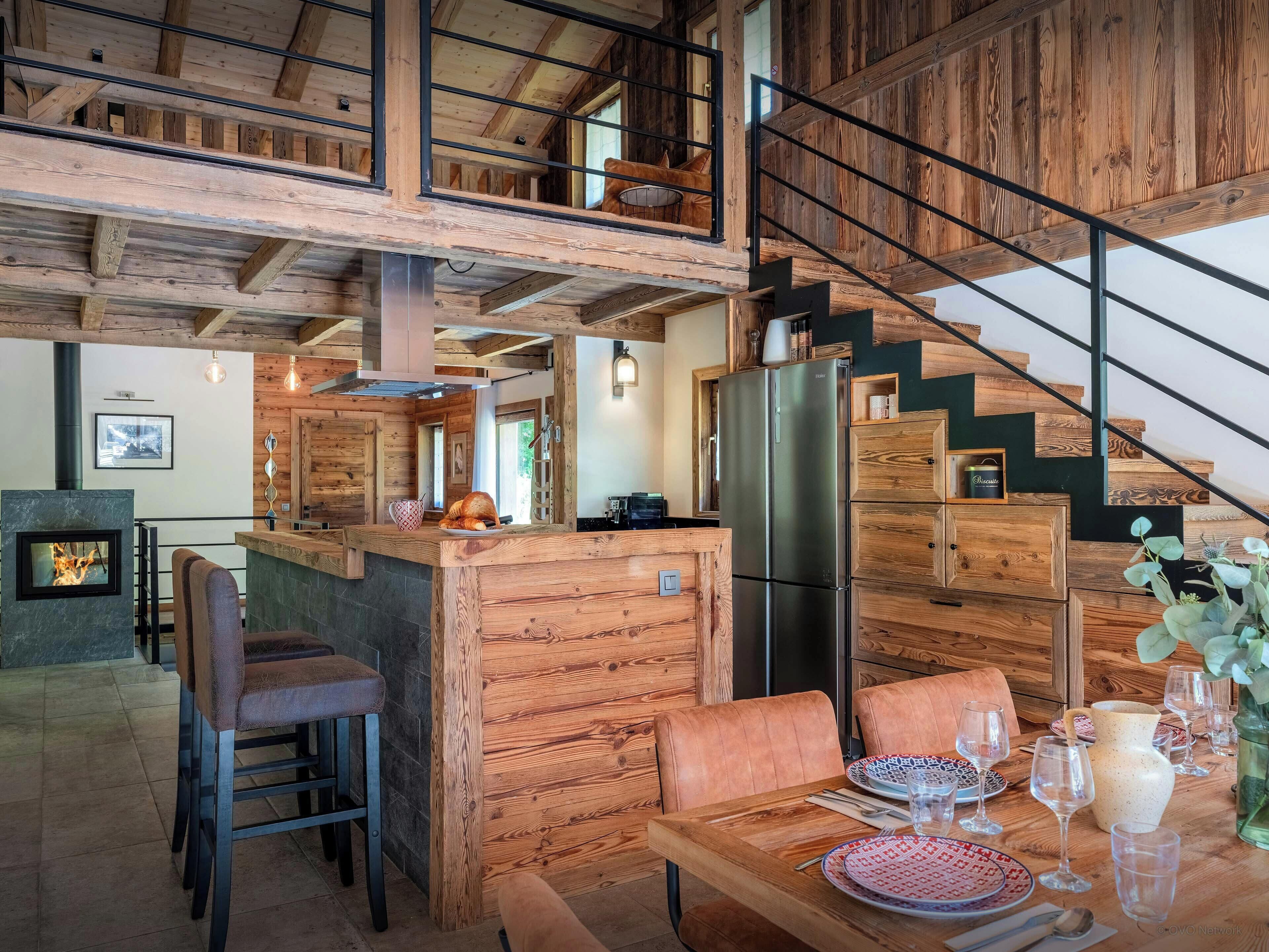 Une cuisine moderne dotée d’un réfrigérateur en acier inoxydable, de meubles en bois et d’un coin repas avec une table et des chaises en bois.