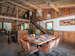 A wooden interior with a dining table set for six, surrounded by leather chairs, a staircase, and a modern kitchen in the background. - Chalet Amontis - Peaceful chalet with premium facilities - OVO Network (Saint-Gervais-les-Bains)