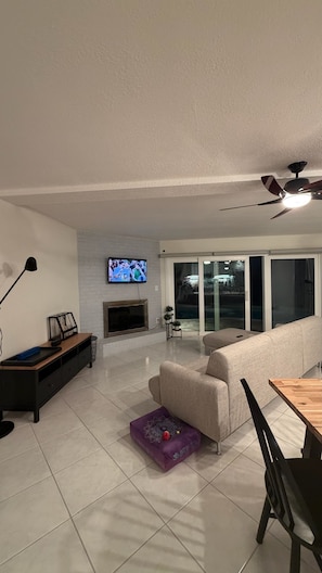 A living room with a sofa, a TV mounted on the wall, a fireplace, a ceiling fan, and a dining area with a table and chairs. - Beach House in Indian Rocks Beach | 4 bedrooms with pool (Indian Rocks Beach)