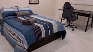 Une chambre à coucher avec un lit, un bureau, une chaise, un ventilateur de plafond et une affiche accrochée au mur.