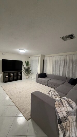 A living room with a flat-screen TV, a grey sofa, a patterned throw blanket, and a potted plant. - Beach House in Indian Rocks Beach | 4 bedrooms with pool (Indian Rocks Beach)