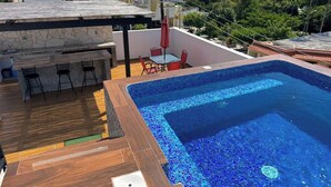 Piscina no terraço com deck ladrilhado, área de bar e vista para o horizonte da cidade.