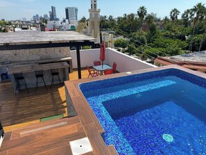 A rooftop swimming pool with a tiled deck, a bar area, and a view of the city skyline. - Modern Condo in Gabbiani, by GPS (Mazatlán)