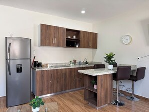 A modern kitchen with a built-in refrigerator, wooden cabinets, a granite countertop, and a small island with bar stools. - Modern Condo in Gabbiani, by GPS (Mazatlán)