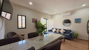 Uma sala de estar moderna com área de jantar, um sofá, uma planta em vaso e uma TV de tela plana na parede.
