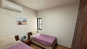 Quarto com duas camas, piso de madeira, guarda-roupa, janela e ar condicionado.
