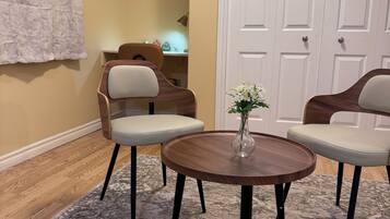 Um quarto com uma mesa de madeira redonda, duas cadeiras, um vaso com flores, uma pintura de Buda e uma porta branca.