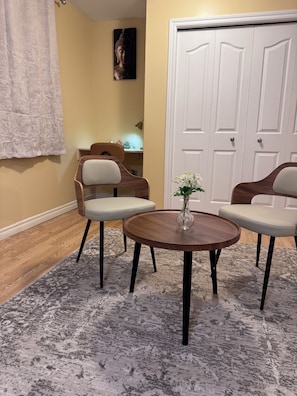 Een kamer met een ronde houten tafel, twee stoelen, een vaas met bloemen, een Boeddha-schilderij en een witte deur.