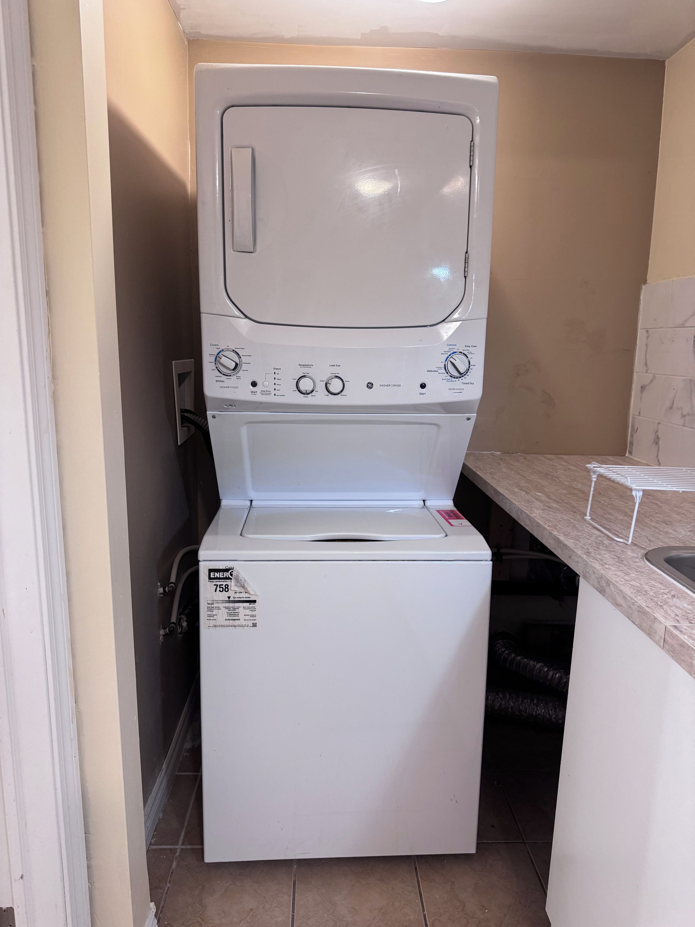 A compact washer and dryer unit with a control panel, located in a small laundry room with tiled flooring.