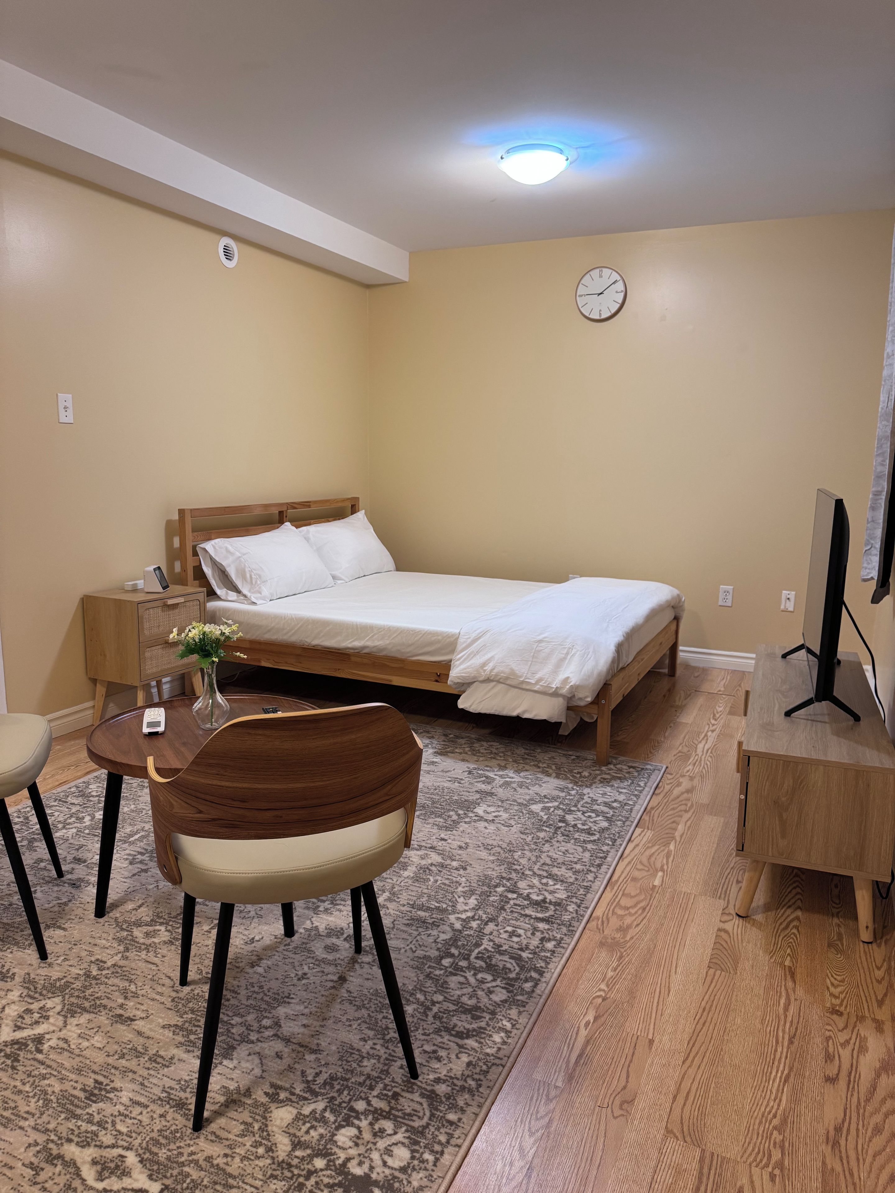 Une chambre d’hôtel avec un lit, une table de chevet, une chaise, un bureau et une horloge au mur.