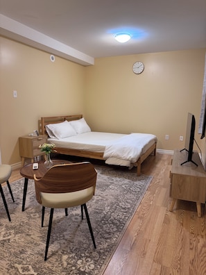 Una habitación de hotel con cama, mesita de noche, silla, escritorio y un reloj en la pared.