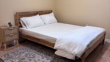 A single bed with a wooden frame and white bedding, a bedside table with a lamp, and a wall clock.