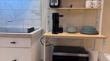 Cozinha equipada com micro-ondas, cafeteira e um armário com cápsulas de café e xícaras.