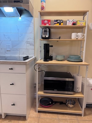 Een keuken met een magnetron, koffiezetapparaat en een plank met koffiekapsules en bekers.