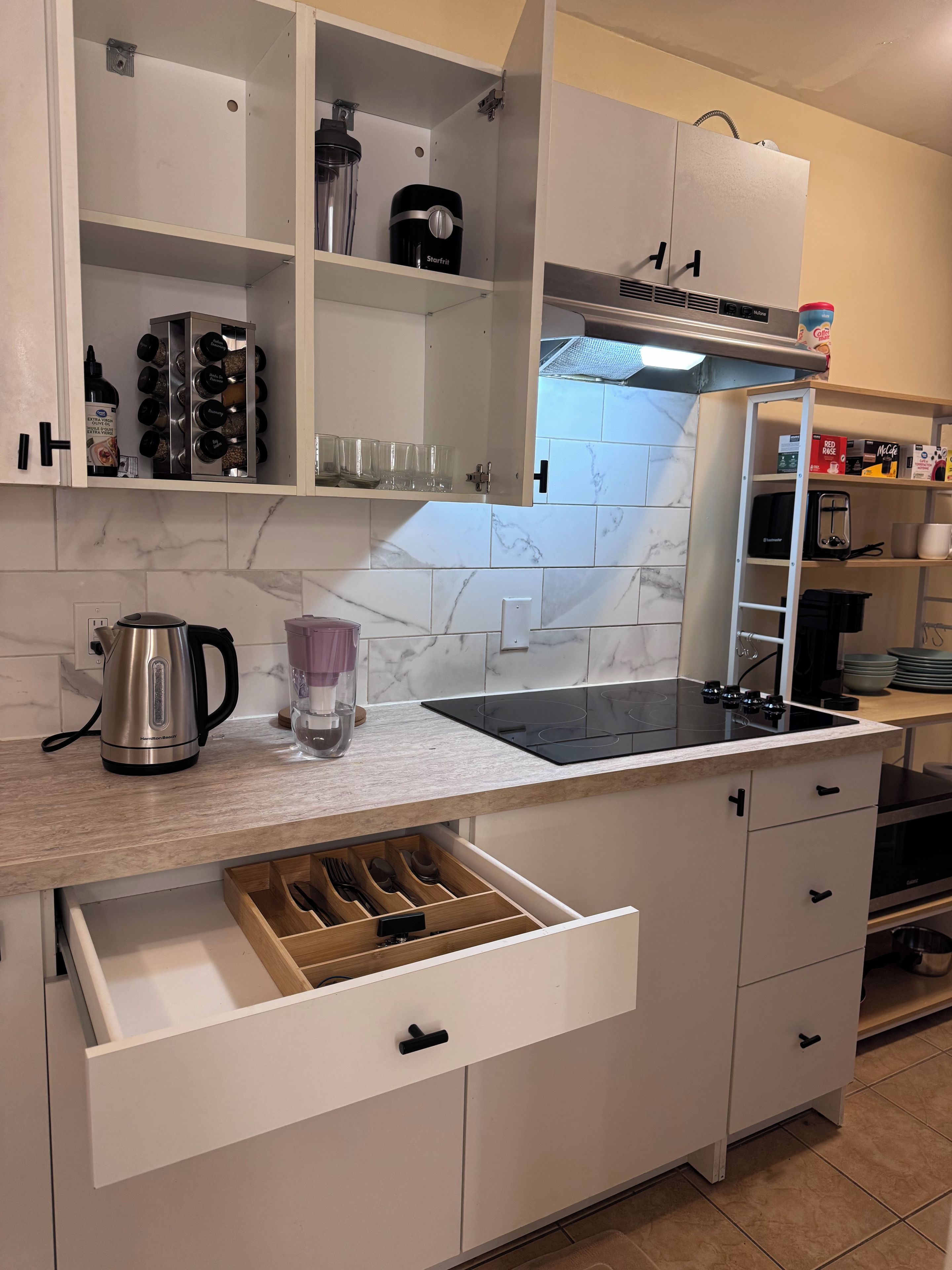 Une cuisine moderne avec des meubles blancs, un pare-feu en marbre, une bouilloire en acier inoxydable, un mixeur et une machine à café.