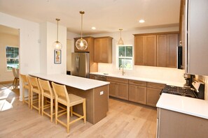 Una cocina moderna con armarios de madera, un refrigerador de acero inoxidable, una encimera blanca y una zona de bar con sillas de madera.