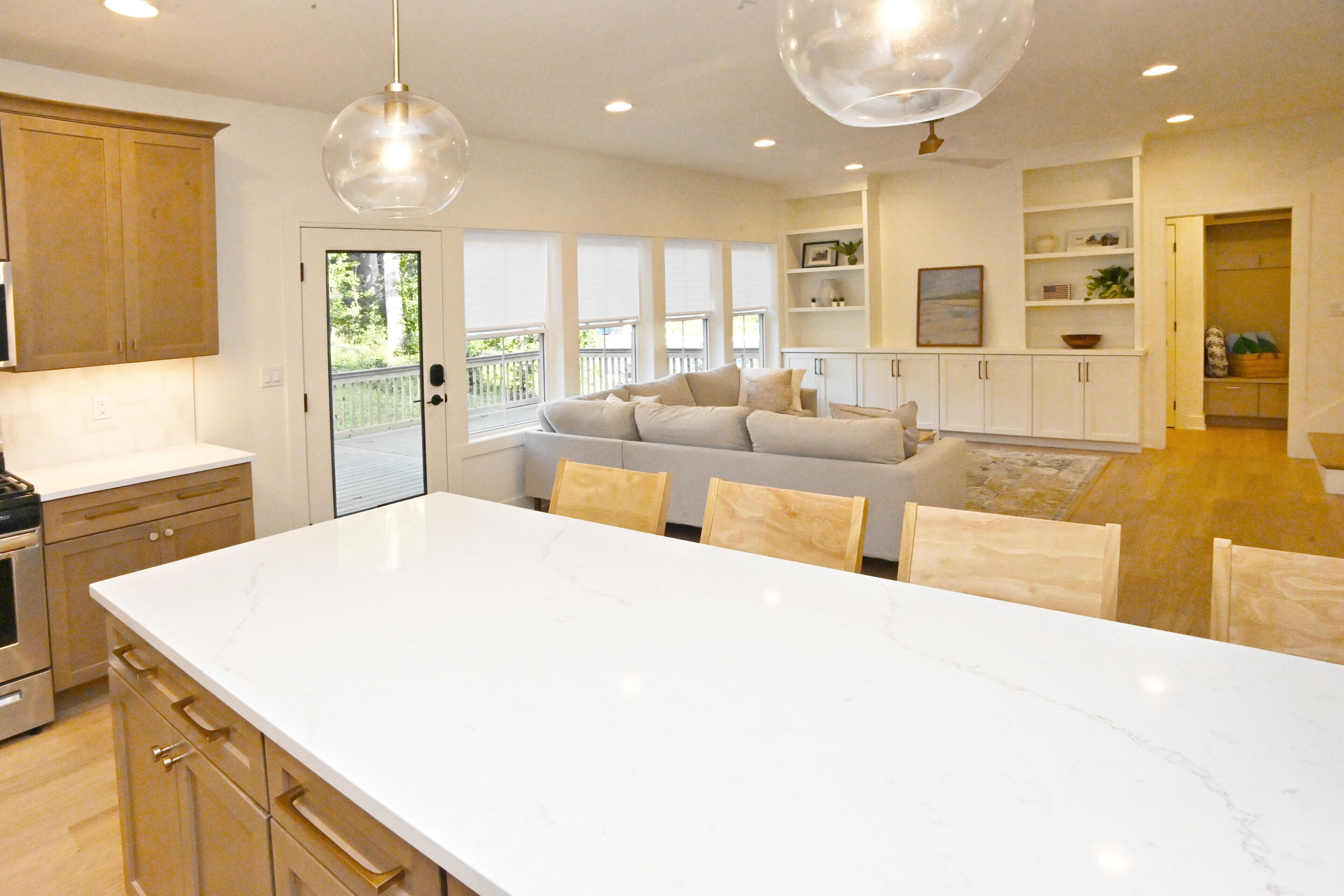A modern kitchen with a large island, wooden cabinets, and pendant lighting.