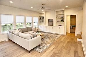 A modern living room with a sectional sofa, a coffee table, and a patterned rug. There are built-in cabinets and a ceiling fan.