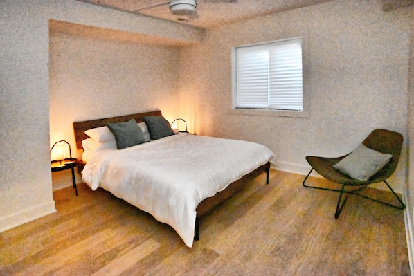 A bedroom with a bed, bedside lamps, a chair, a window, and a ceiling fan.