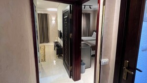 Un pasillo de hotel con una alfombra estampada, una cama, un escritorio y un baño a la vista.