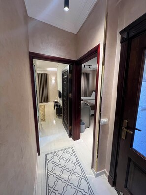 Ein Hotelkorridor mit Teppichmuster, einem Bett, einem Schreibtisch und einem im Hintergrund sichtbaren Badezimmer.