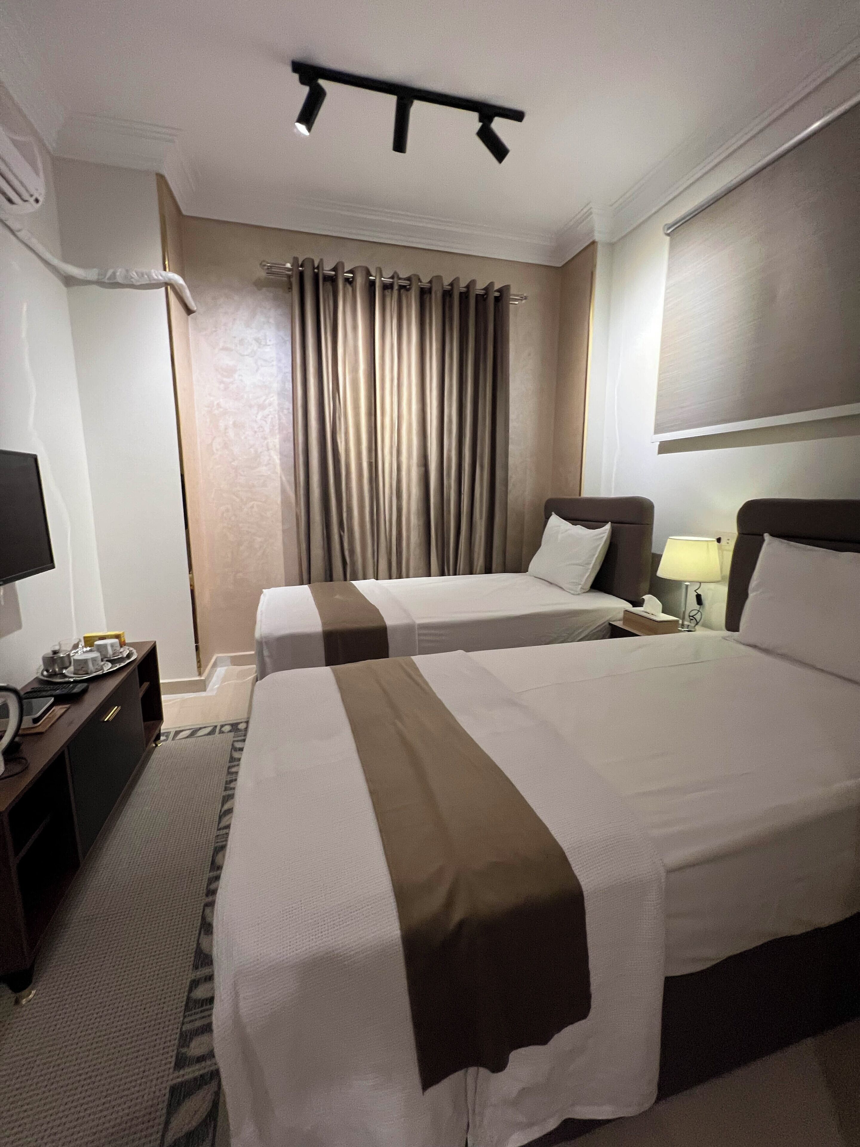 A hotel room with two beds, a desk with a lamp, a TV, and a curtain.