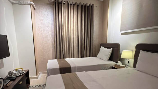 Habitación de hotel con dos camas, un escritorio con lámpara, televisión y cortina.