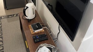 Habitación de hotel con televisor de pantalla plana montado en la pared, cafetera, control remoto y bandeja con tazas y un vaso.