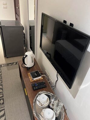 Ein Hotelzimmer mit flachbildfernseher an der Wand, einer Kaffeemaschine, einer Fernbedienung und einem Tablett mit Tassen und einem Glas.