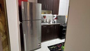 Una cocina con piso de baldosas blancas, gabinetes de madera oscura, un refrigerador de acero inoxidable y una estufa negra.