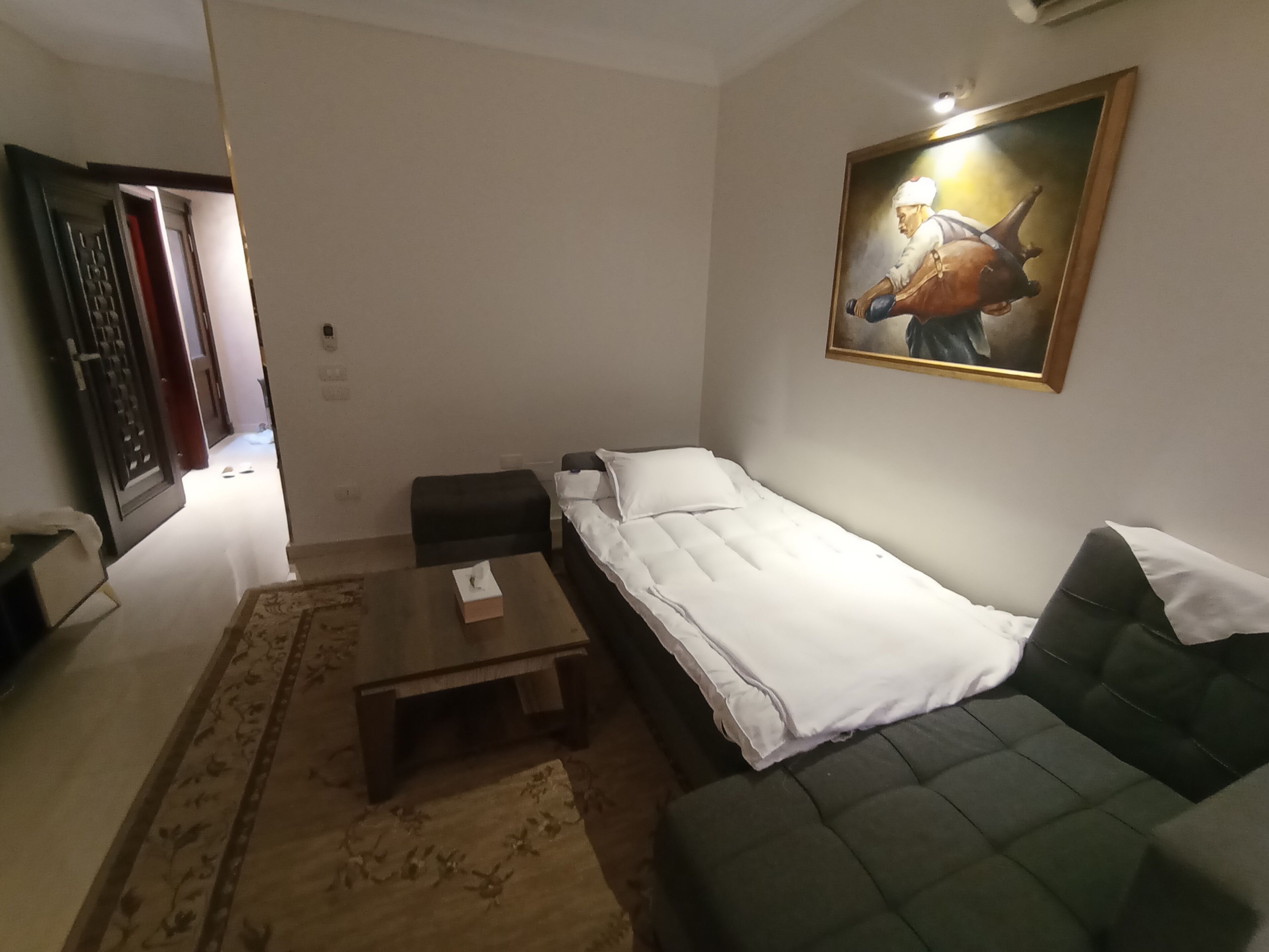 Een knus woongedeelte met een bed, een bank, een klein tafeltje en een schilderij aan de muur.
