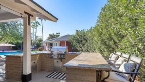 An outdoor kitchen area with a grill, seating, and a view of a swimming pool. - Private Scottsdale Oasis - Pool, Spa & Casita (Scottsdale)