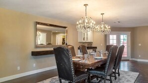 A dining room with a wooden table, four upholstered chairs, a chandelier, a large mirror, and a door leading outside. - Private Scottsdale Oasis - Pool, Spa & Casita (Scottsdale)