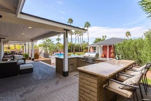 Un patio exterior con una parrilla, zona de estar y vistas a una piscina.