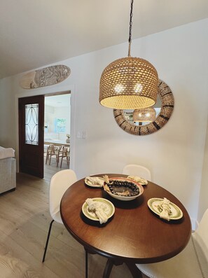A dining area with a round table, chairs, and a hanging light fixture. - The Tidal Retreat | 2BD 1BA (St. Augustine)