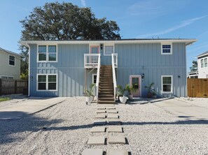 A two-story house with a front porch, a staircase, and a driveway. - The Tidal Retreat | 2BD 1BA (St. Augustine)