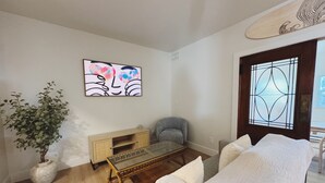 Un salon comprenant un canapé, une table basse avec un plateau en verre, un fauteuil gris, un meuble en bois et une plante en pot.