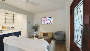 Une pièce comprenant un lit, une chaise, une petite table, une plante en pot, un four à micro-ondes et une fenêtre ornée de vitraux.