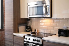 A modern kitchen with a stainless steel stove, a microwave, and a blender on the counter. - Downtown Dallas Haven | Pool + Theater + Game Room (Dallas)