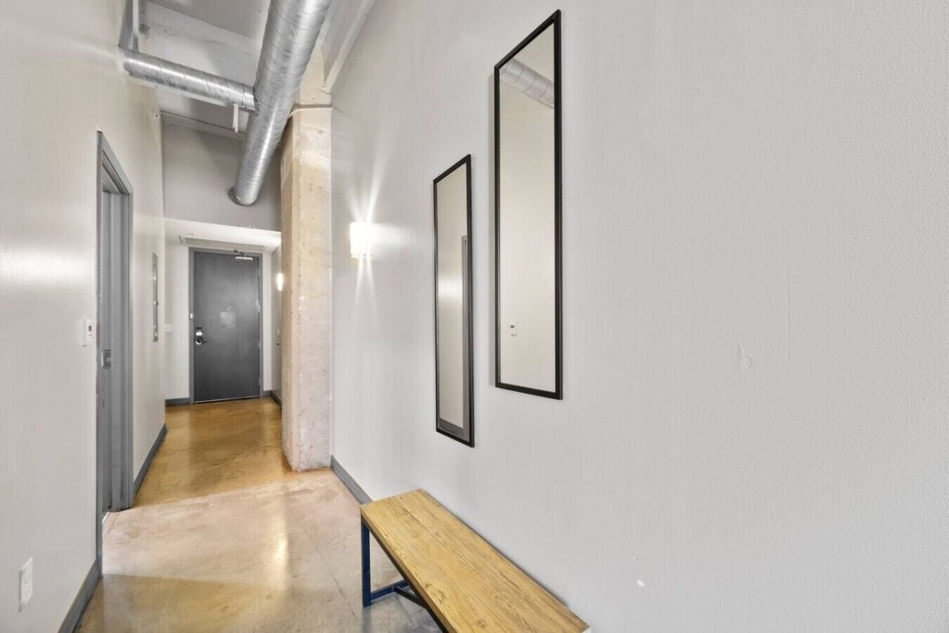 A hallway with a bench, a door at the end, and two framed pictures on the wall.