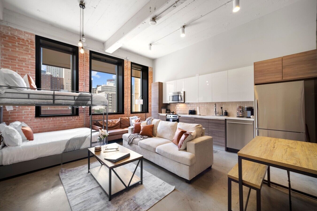A modern apartment with a loft-style bed, a sofa, a dining table, and a kitchen area.