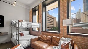A bunk bed with white bedding and a brown leather couch with pillows. - Downtown Dallas Haven | Pool + Theater + Game Room (Dallas)
