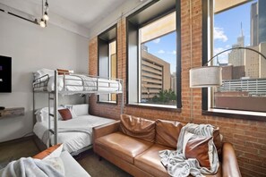 A bunk bed with white bedding and a brown leather couch with pillows. - Downtown Dallas Haven | Pool + Theater + Game Room (Dallas)