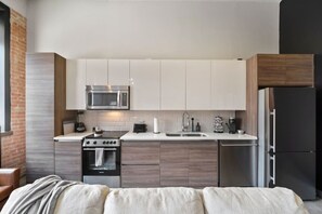 A modern kitchen with a stove, microwave, sink, and refrigerator. - Downtown Dallas Haven | Pool + Theater + Game Room (Dallas)