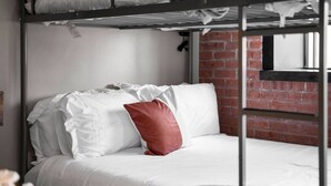 A bunk bed with white bedding and a red pillow, a brick wall, and a window. - Downtown Dallas Haven | Pool + Theater + Game Room (Dallas)