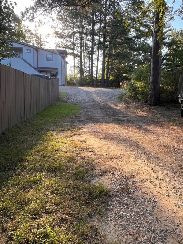 A gravel driveway leading to a house with a wooden fence and trees in the background.