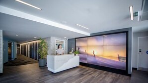 A modern reception area with a reception desk, a large wall mural, and a potted plant. - Mi-pad Smart Hotel (Queenstown)