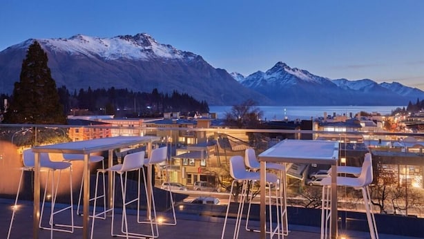 A rooftop bar with tables and chairs, overlooking a mountain range and a body of water. - Mi-pad Smart Hotel (Queenstown)